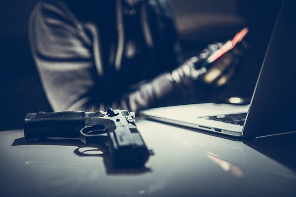 Банда хакеров. Пистолет и ноутбук на столе. Концепция киберпреступности
.