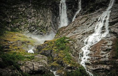 Kısa çalılar ve en az yeşillik ile çevrili dramatik Norveç Şelalesi manzarası.