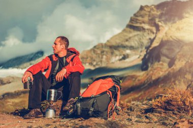 Beyaz erkek yürüyüşçü yüksek dağa tırmandıktan sonra dinleniyor ve sıcak içecek içiyor.. 