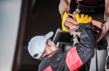 İki İnşaat Erkek İşçisi Turuncu Seramik Çatı Döşemesini Boşaltıyorlar ve Malzeme İş Alanının Yakınına Yerleştiriyorlar. 