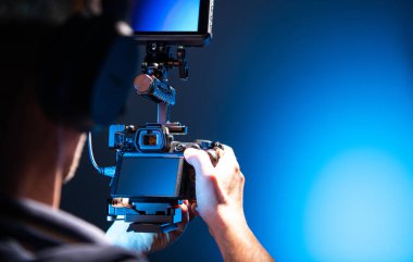 Modern Dijital SLR Kamera in Hands ve Ek Geniş Ekran ile Video Kamera Operatörü. Videografi Teması. Stüdyoda Koyu Mavi Işık.