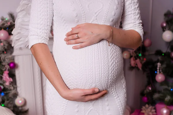 Schwangere Mädchen im weißen Kleid umarmt ihren Bauch. — Stockfoto