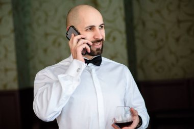 A bald man speaks on the phone in the restaurant. clipart