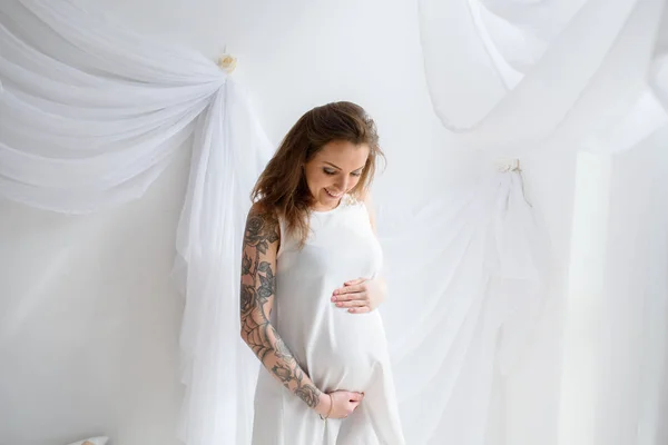 Hermosa chica embarazada con tatuaje en vestido blanco . —  Fotos de Stock