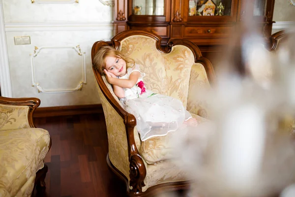 Menina bonita com cachos e vestidos brancos Quinceanera com um trem deitado em um assento rosa e divertido balança as pernas — Fotografia de Stock