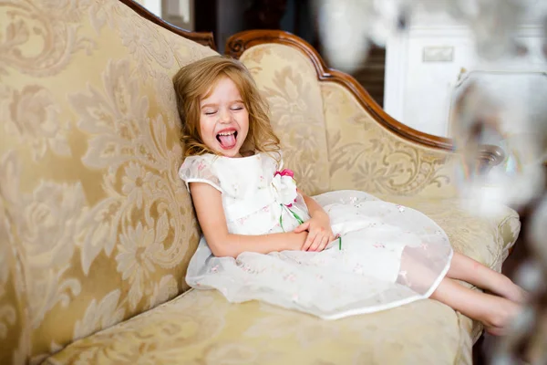 Egy szőke kislány ül a nagy kanapé színes öltöztetős. — Stock Fotó