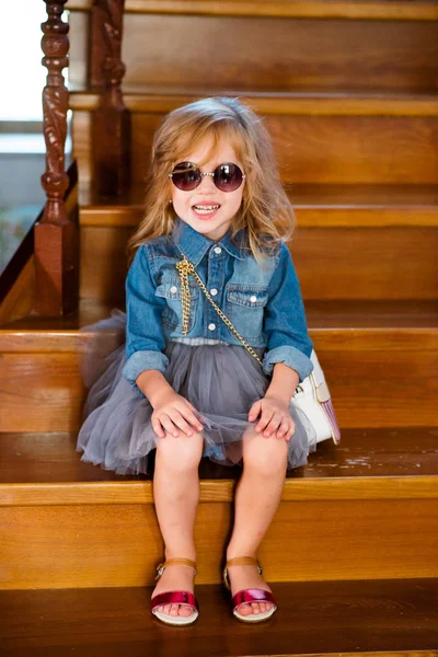 Niña con camisa vaquera y gafas de sol posando y sonriendo . —  Fotos de Stock