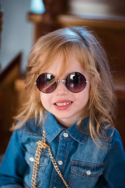 Bambina in jeans camicia e occhiali da sole in posa e sorridente . — Foto Stock