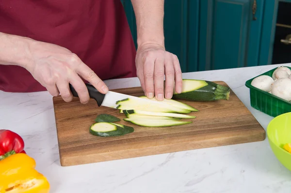 Closeup of sliced zucchini on table. Close up of hands slicing green vegetable with white knife. Closeup of men cutting green zucchini on wooden board
