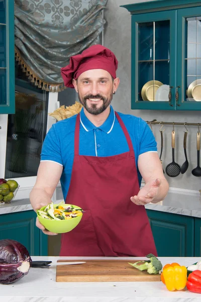 Kırmızı önlük ve şapka şef salatası yaptı. Şapkalı adam yeşil plaka salata ile mutfak ellerinde tutar. Profesyonel Chef mutfak pişirme sebze salatası. Sarı plaka salata ile. Erkekler deneyin salata öneriyor