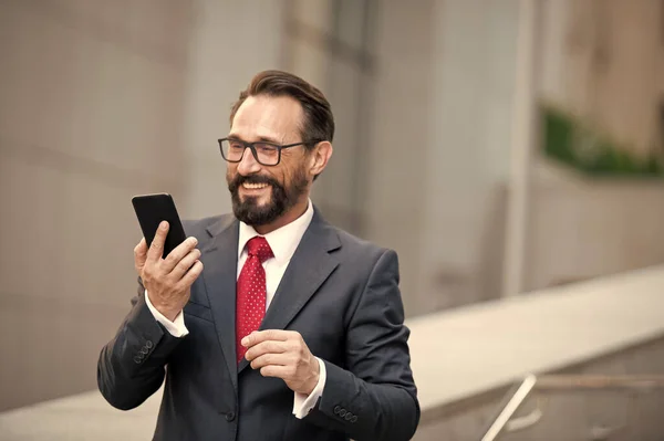 Gözlüklü bir iş adamı ofis girişinde şehir geçmişine sahip akıllı bir telefon kullanıyor. İş adamlarının teknolojiyi kullanması. Takım elbiseli adam internet üzerinden cep telefonuyla bilgi topluyor.