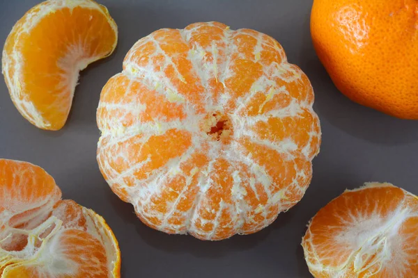 Closeup of peeled and unpeeled whole mandarin and pieces on a grey background — Stock Photo, Image