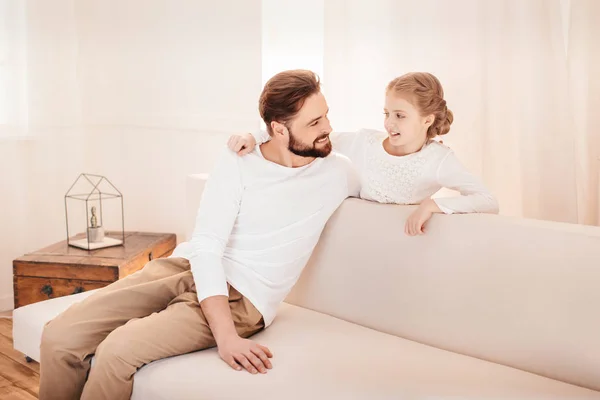 Sevimli küçük kız ile birlikte kanepede oturan ve birbirlerine gülümseyen baba — Stok fotoğraf