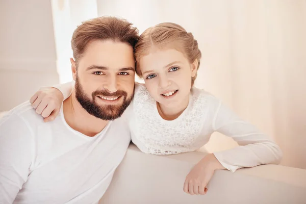 Портрет очаровательной маленькой девочки, обнимающейся с отцом и улыбающейся в камеру — стоковое фото