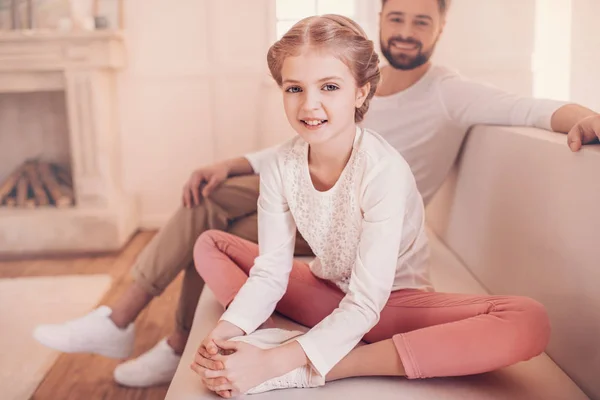 Cute little girl with father sitting on sofa and smiling at camera — Stock Photo, Image