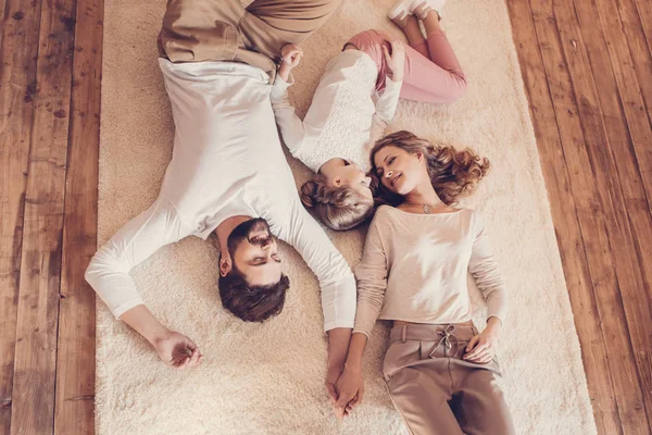 Visão superior da família feliz com uma criança deitada juntas no tapete — Fotografia de Stock