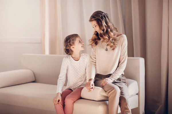 Gyönyörű anya és lánya együtt ül a kanapén, és mosolyogva egymást — Stock Fotó