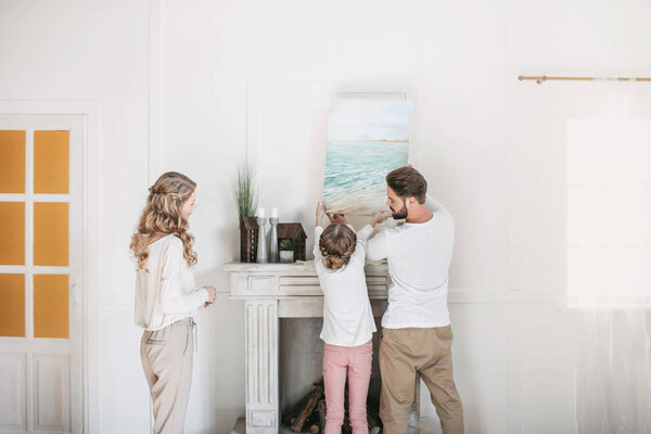Happy family hanging picture of sea over the fireplace at home