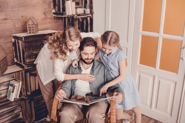 daughter, mother and father sitting in rocking chair and reading book