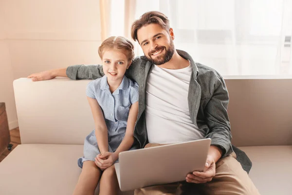 Happy father and daughter sitting on sofa and using laptop at home — Stock Photo, Image