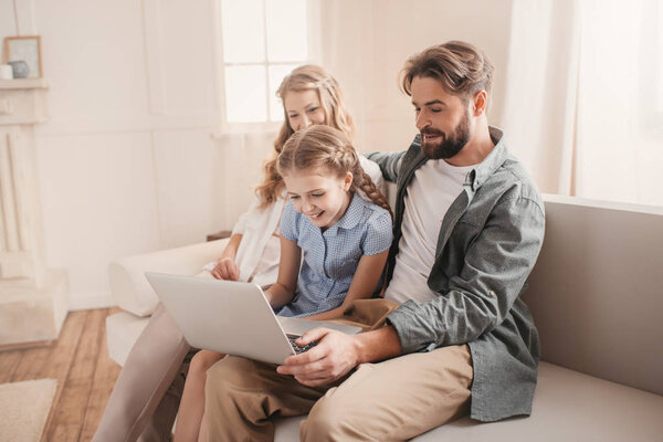 Happy family sitting on sofa and using laptop at home 