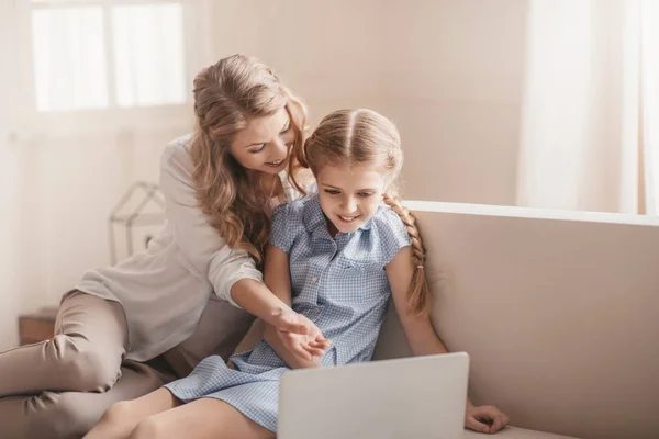 Счастливые мать и дочь сидят на диване и пользуются ноутбуком дома — стоковое фото