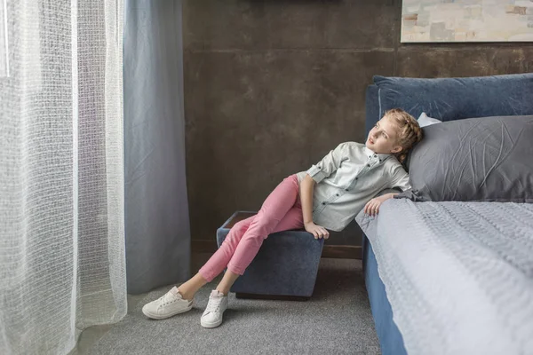Fundersam bedårande flicka sitter på puffen nära sängen hemma — Stockfoto