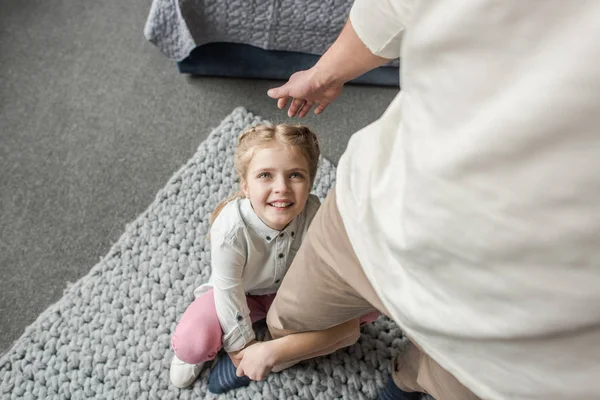 Happy adorable daughter sitting on floor and hugging father's leg — Stock Photo, Image