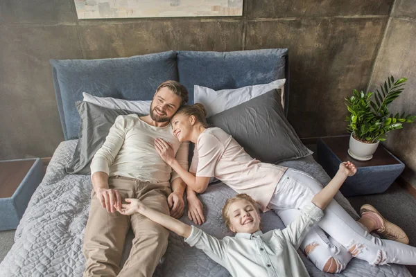 Feliz adorable hija con madre y padre relajándose en la cama en casa —  Fotos de Stock