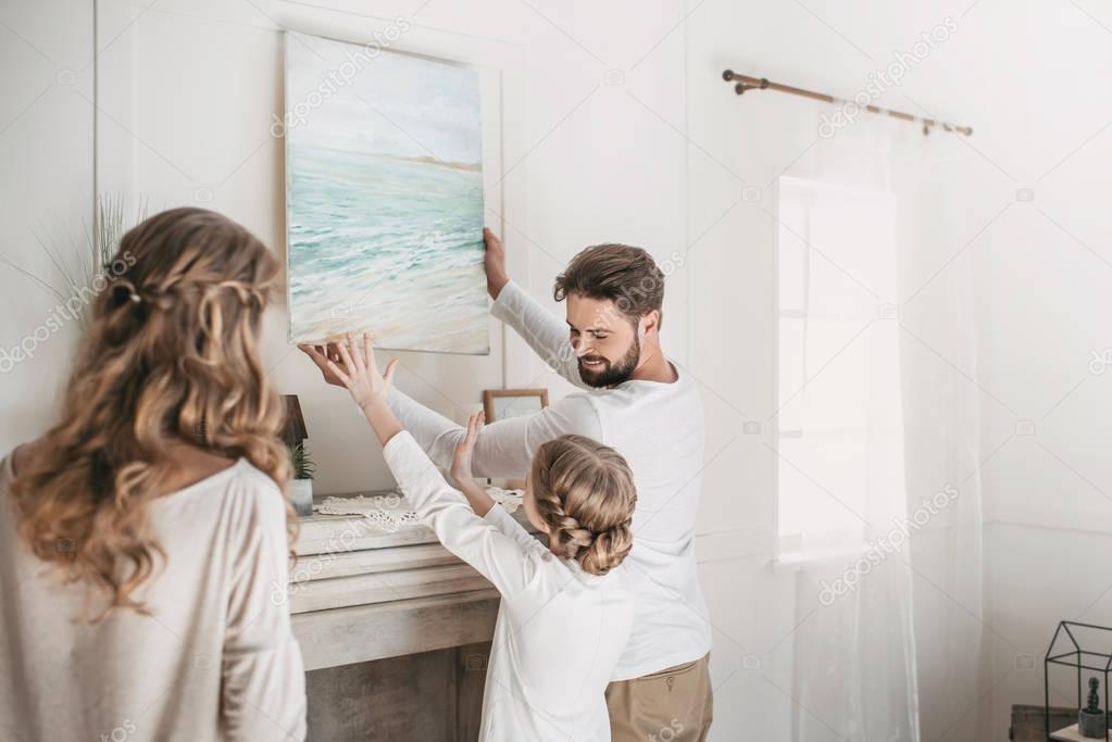 Happy family hanging picture of sea over the fireplace at home