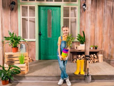 Renkli saksı ev bitki ile tutarak ve kameraya gülümseyen sevimli küçük kız 