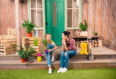 Mutlu anne ve kızı ile birlikte verandada oturup ve birbirlerine gülümseyen Saksılı bitki