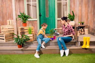 Mutlu anne ve kızı verandada oturup ve bitki sulama