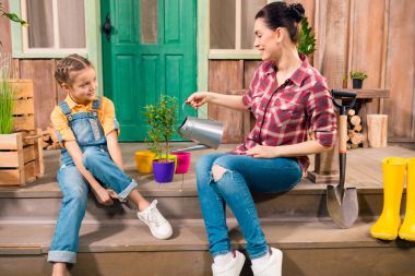 Gülümseyen anne ve verandada oturup ve bitki sulama kızı yan görünüm