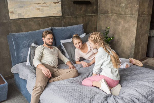 happy adorable daughter with mother and father relaxing on bed at home