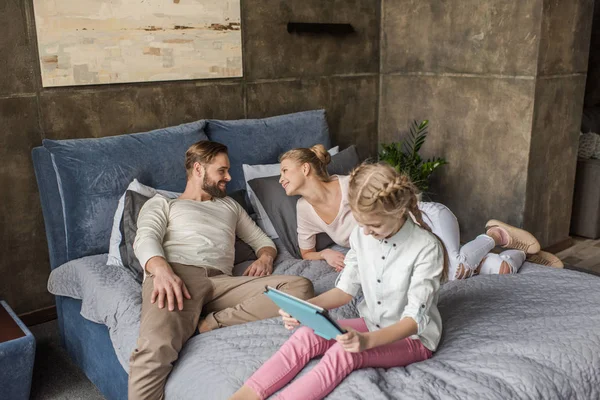 Schattige dochter met behulp van digitale tablet en liggend op bed met ouders — Stockfoto
