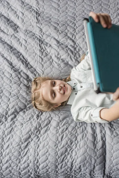 Adorable fille en utilisant tablette numérique et couché sur le lit à la maison — Photo gratuite