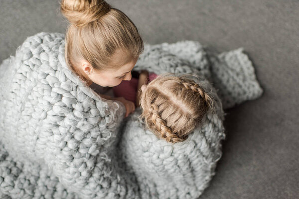 overhead view of mother and daughter hugging and sitting on floor with wool knitted blanket