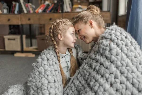 Beautiful happy mother and daughter sitting together under merino wool blanket — Stock Photo, Image