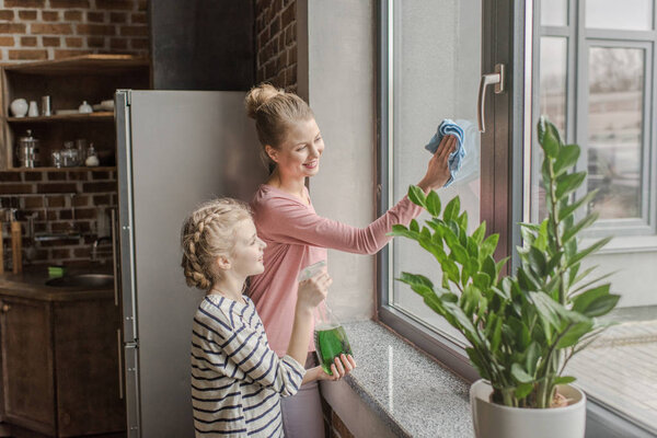 Happy mother and daughter cleaning window with rag and spray bottle together