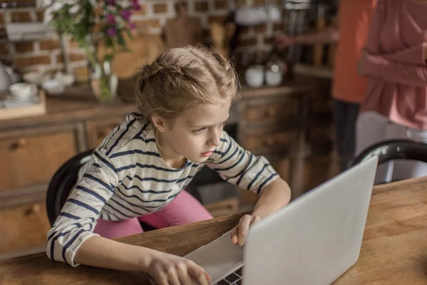 Konzentriertes kleines Mädchen mit Laptop auf Holztisch — kostenloses Stockfoto