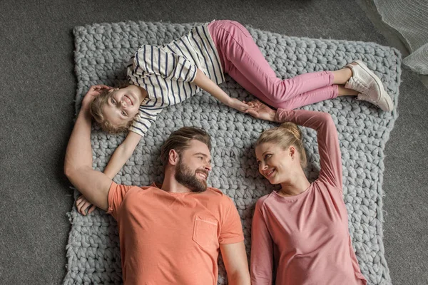 Visão superior da família feliz com uma criança deitada em conjunto no tapete de malha cinza — Fotografia de Stock