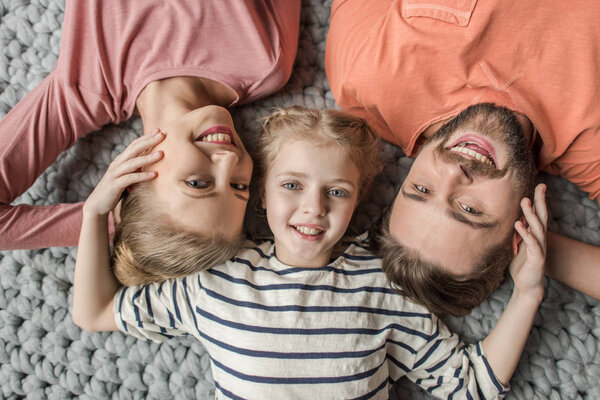 Top view of happy family with one child lying together on grey knitted carpet