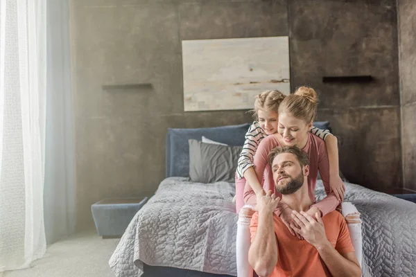 Счастливая молодая семья с одним ребенком, сидящая вместе и обнимающаяся в спальне — стоковое фото