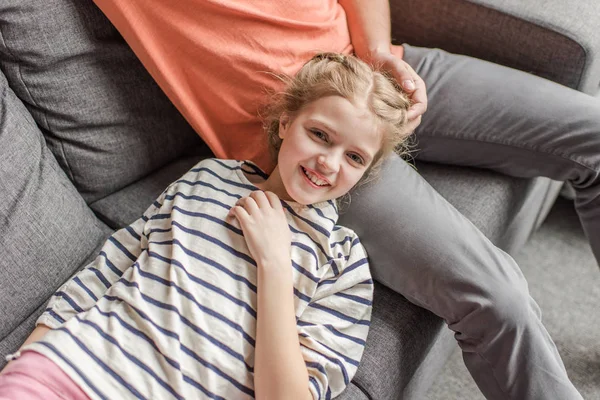 Happy little girl lying on father legs and smiling at camera — Stock Photo, Image