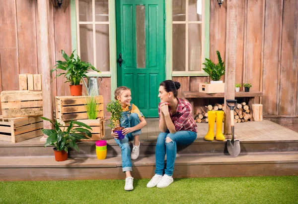 Happy mother and daughter with potted plant sitting together on porch and smiling each other — Stock Photo, Image