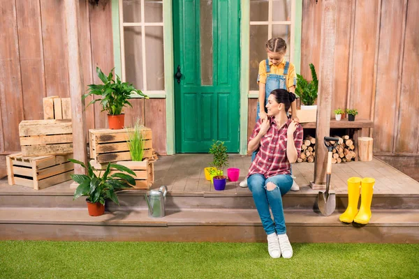 Feliz madre e hija abrazándose en el porche con plantas en maceta — Foto de Stock