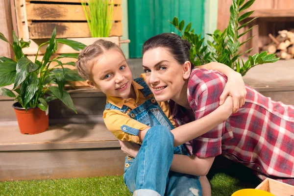 Glückliche Mutter und Tochter umarmen sich auf grünem Rasen und lächeln in die Kamera — kostenloses Stockfoto