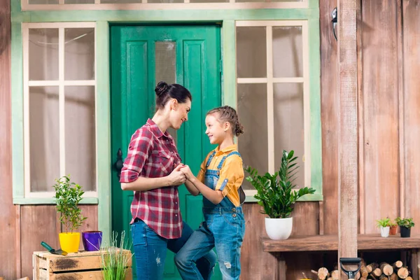 Happy mother and daughter standing together and holding hands on porch — Stock Photo, Image