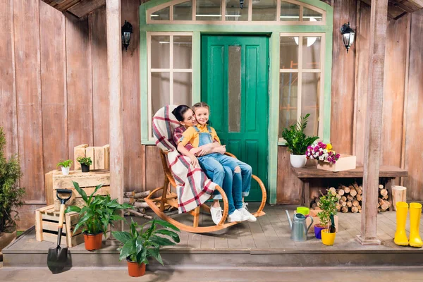 Mother and daughter sitting in rocking chair and hugging on porch — Stock Photo, Image